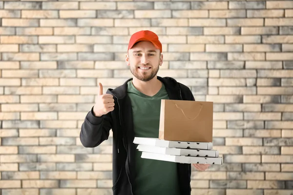 Karton pizza kutuları ve kağıt torba tuğla duvar arka plan üzerinde olan genç adam. Gıda dağıtım hizmeti — Stok fotoğraf