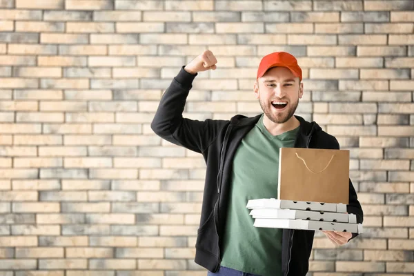 Jeune homme avec boîtes à pizza en carton et sac en papier sur fond de mur de briques. Service de livraison de nourriture — Photo