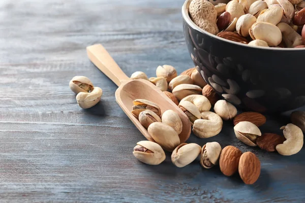 Bowl and scoop with different nuts on wooden table — Stock Photo, Image