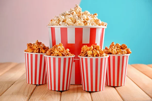 Tassen mit leckerem Popcorn auf dem Tisch vor farbigem Hintergrund — Stockfoto
