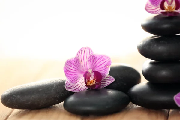 Pietre termali con bellissimi fiori di orchidea sul tavolo di legno Foto Stock Royalty Free