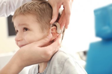 Otolaryngologist putting hearing aid in little boy's ear indoors clipart
