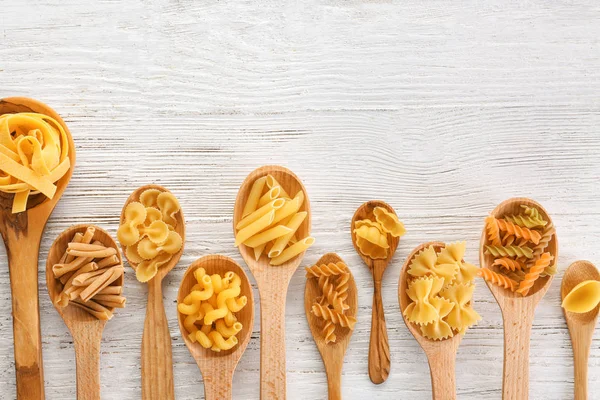 Wooden spoons with uncooked pasta on light background — Stock Photo, Image