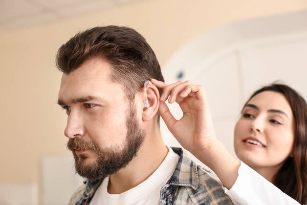 Отоларинголог помещает слуховой аппарат в ухо человека на светлом фоне
