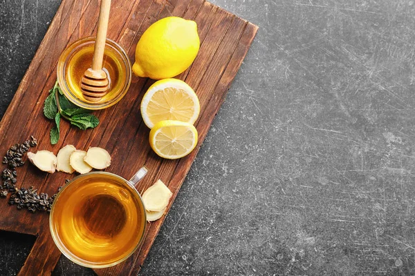 Delicious tea with honey, lemon and ginger on grey background — Stock Photo, Image