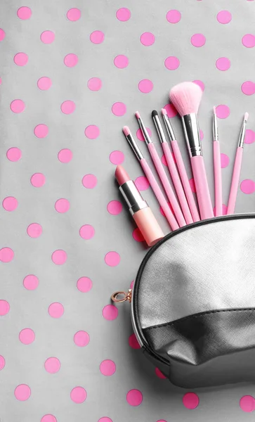 Cosmetic bag with different brushes of professional makeup artist and lipstick on color background — Stock Photo, Image