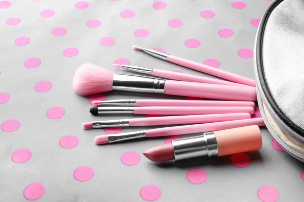 Cosmetic bag with different brushes of professional makeup artist and lipstick on color background — Stock Photo, Image