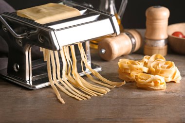 Metal pasta maker with dough on kitchen table clipart