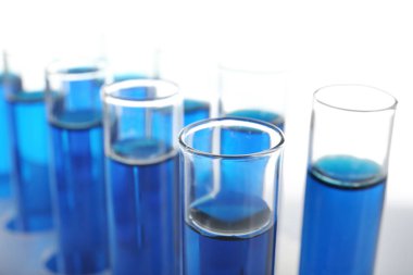 Beyaz zemin üzerinde mavi sıvı bulunan test tüpleri