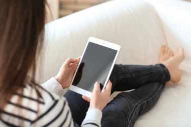 Genç kadın evde koltukta istirahat ederken tablet kullanma