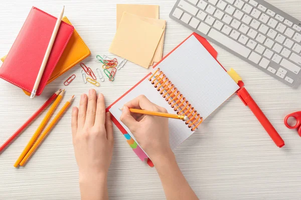 Woman writing in notebook at table, top view. Workplace composition — Stock Photo, Image