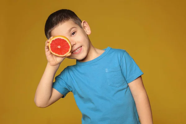 Funny little boy with citrus fruit on color background — Stock Photo, Image