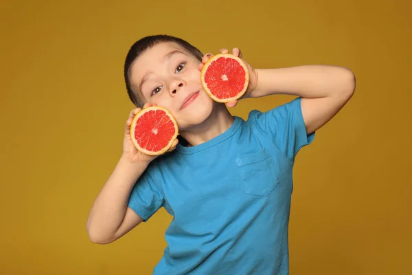Funny little boy with citrus fruit on color background — Stock Photo, Image