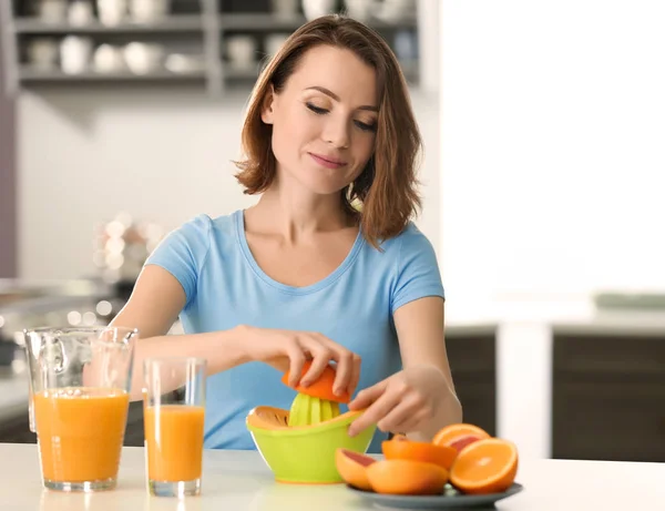 Beautiful woman squeezing citrus juice in kitchen — Stock Photo, Image