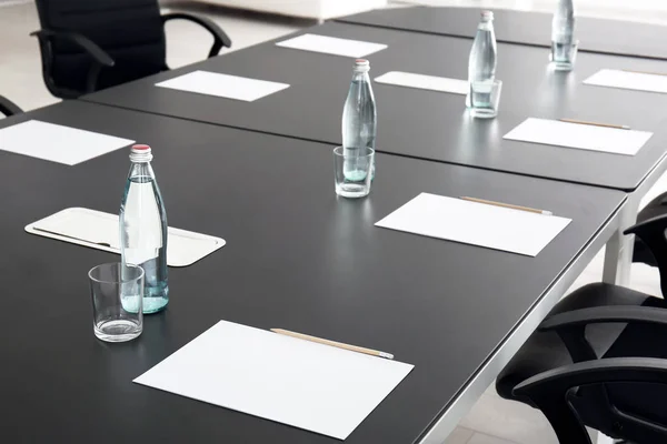 Table with bottles of water and sheets of paper prepared for business meeting in conference hall