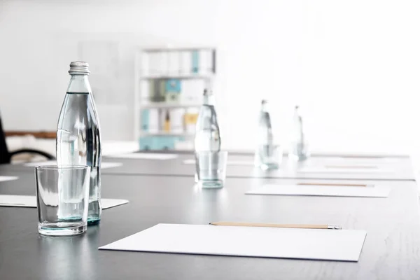 Table with bottles of water and sheets of paper prepared for business meeting in conference hall