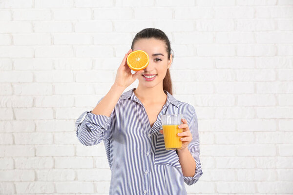 Beautiful young woman with glass of citrus juice and fruit against brick wall