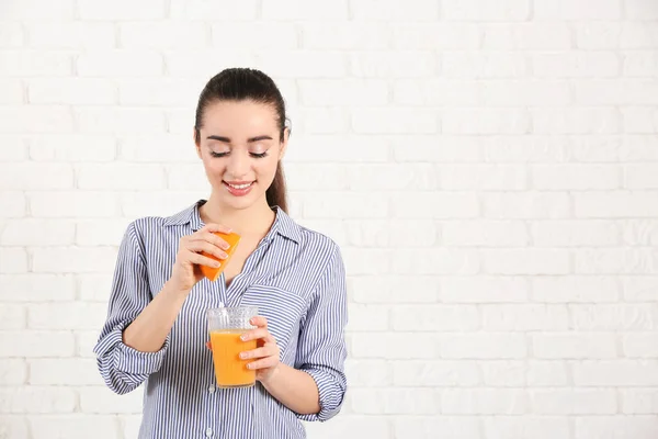 Mooie jonge vrouw met glas sap van citrusvruchten en fruit tegen muur — Stockfoto