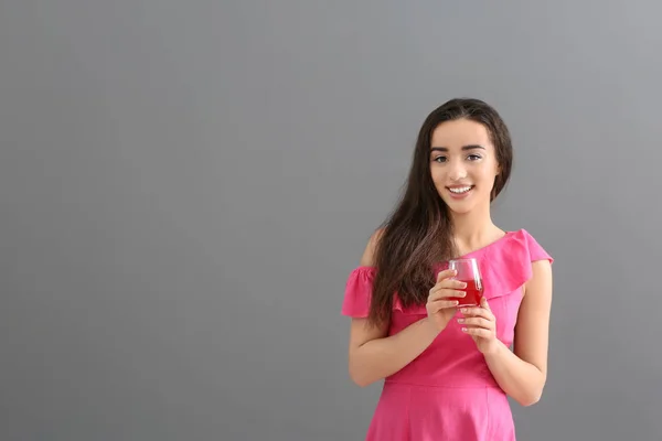 Beautiful young woman with glass of citrus juice on grey background — Stock Photo, Image