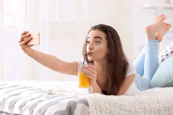 Beautiful young woman taking selfie while drinking citrus juice at home — Stock Photo, Image