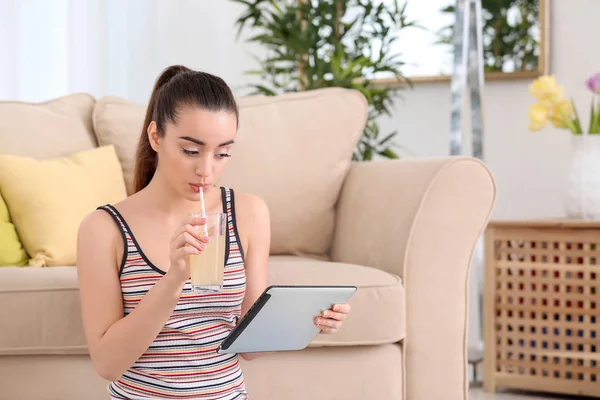 Bella giovane donna con tablet computer che beve succo di agrumi a casa — Foto Stock