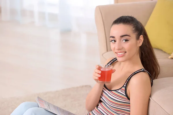 Piękna młoda kobieta w domu do picia soku cytrynowym podczas czytania magazynu — Zdjęcie stockowe