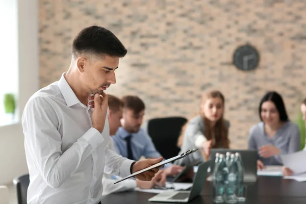 Pensive young man with clipboard at business meeting — Stock Photo, Image