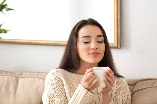 Beautiful young woman with cup of hot tea at home