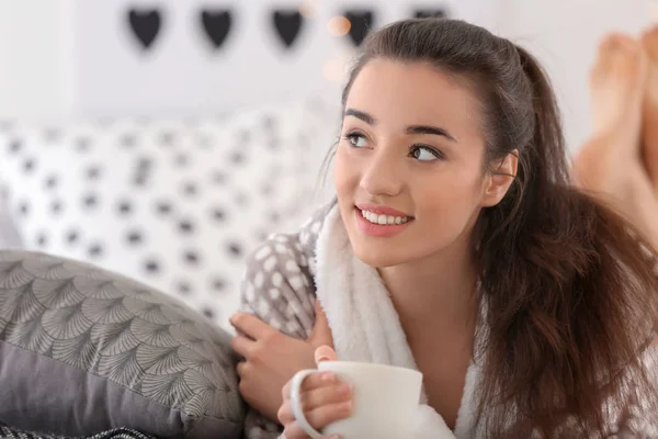 Όμορφη νεαρή γυναίκα με φλιτζάνι καυτό τσάι στο σπίτι — Φωτογραφία Αρχείου