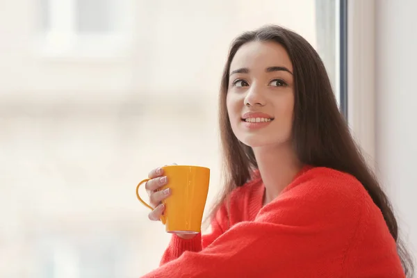 Hermosa joven con taza de té caliente cerca de la ventana en casa — Foto de Stock