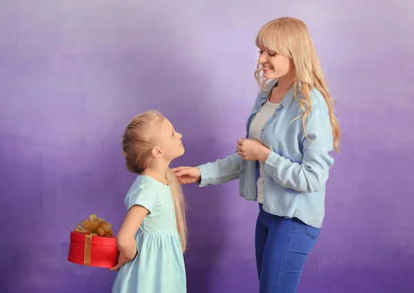 Liten flicka gömmer sig present till mor bakom hennes rygg på färgbakgrund — Stockfoto