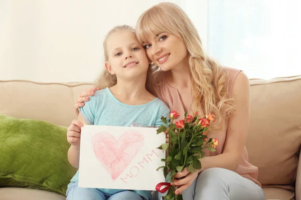 Портрет милой маленькой девочки и ее матери с розовым букетом и поздравительной открыткой дома — стоковое фото