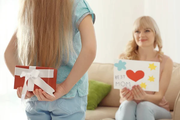 Little girl hiding gift box for mother behind her back at home — Stock Photo, Image