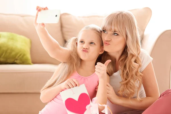 Cute little girl and her mother taking selfie with handmade card at home — Stock Photo, Image