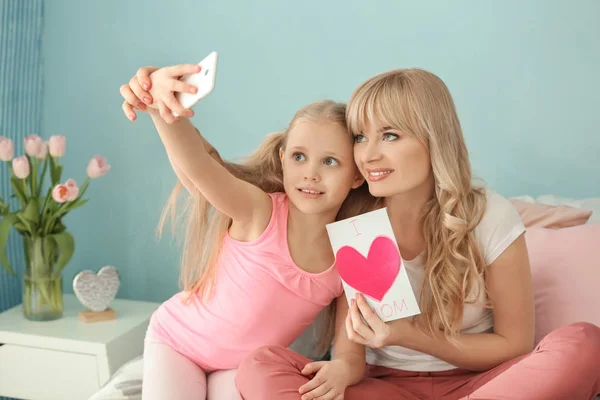 Cute little girl and her mother taking selfie with handmade card at home — Stock Photo, Image