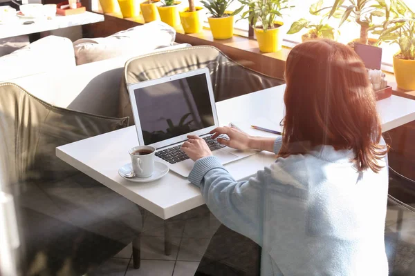 Young woman using laptop in cafe, view through window — Stock Photo, Image