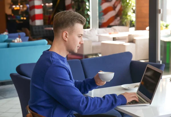 Молодий фрілансер п'є каву під час роботи з ноутбуком за столом у кафе — стокове фото