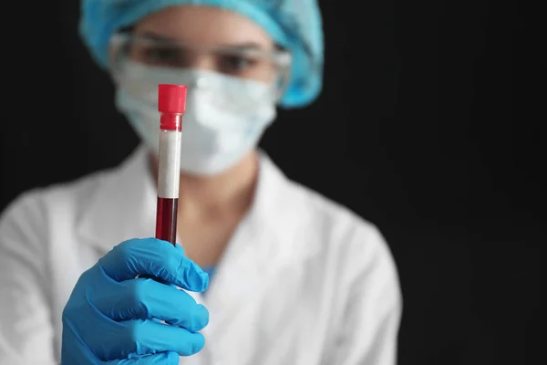 Lab worker holding test tube with blood sample on black background — Stock Photo, Image