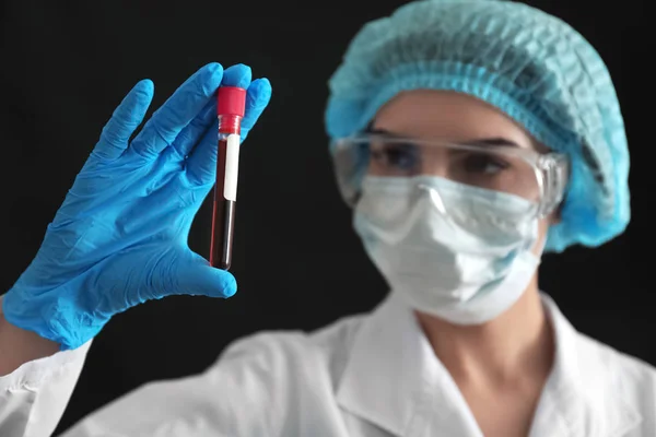 Lab worker holding test tube with blood sample on black background — Stock Photo, Image