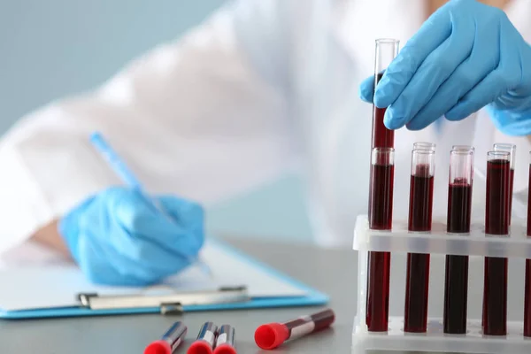 Mujer que trabaja con muestras de sangre en tubos de ensayo en la mesa — Foto de Stock