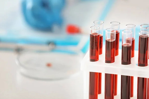 Test tubes with blood samples in holder and blurred lab worker on background — Stock Photo, Image