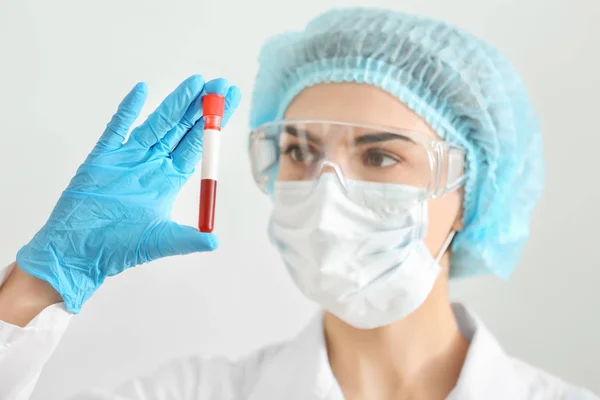 Lab worker holding test tube with blood sample on light background — Stock Photo, Image