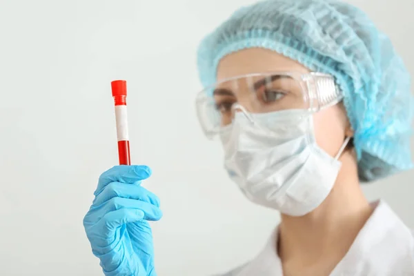 Lab worker holding test tube with blood sample on light background — Stock Photo, Image