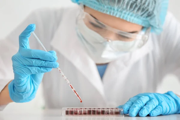 Лаборант капает образцы крови в пробирки за столом — стоковое фото