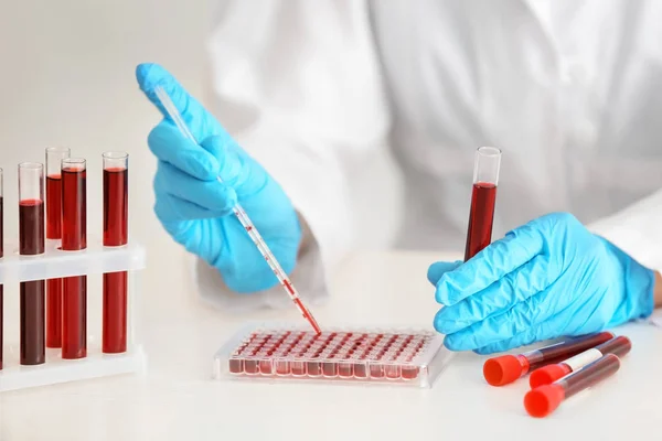 Trabajador de laboratorio que gotea muestras de sangre en tubos de ensayo en la mesa — Foto de Stock