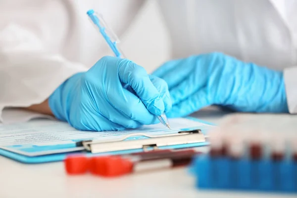 Trabajador de laboratorio llenando formulario cerca de tubos de ensayo con muestras de sangre en la mesa — Foto de Stock