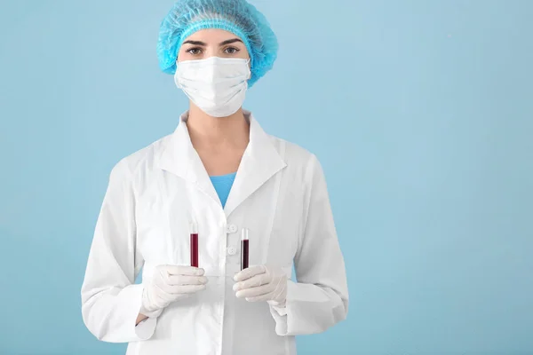 Lab worker holding test tubes with blood sample on color background — Stock Photo, Image