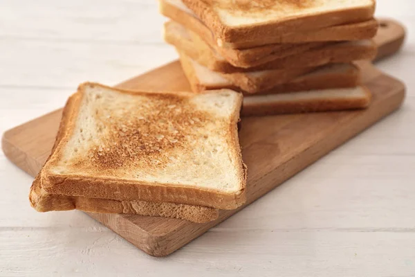 Tabla de madera con sabroso pan tostado en la mesa —  Fotos de Stock