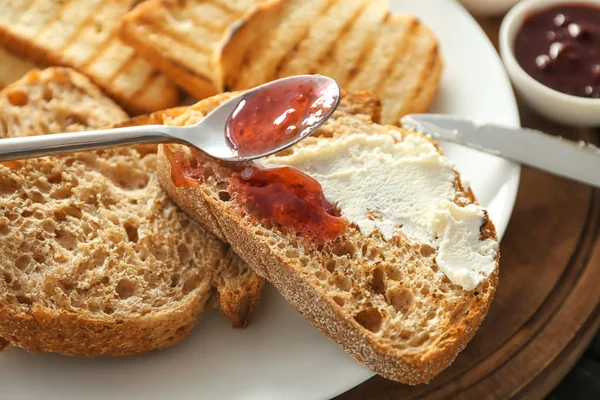 Espalhando o engarrafamento no pão torrado com o queijo de creme, closeup — Fotografia de Stock