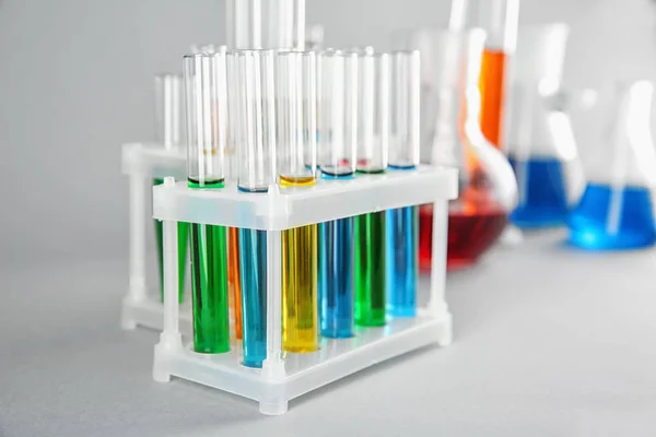 Tubos de ensayo con líquidos de colores en soporte sobre fondo claro — Foto de Stock